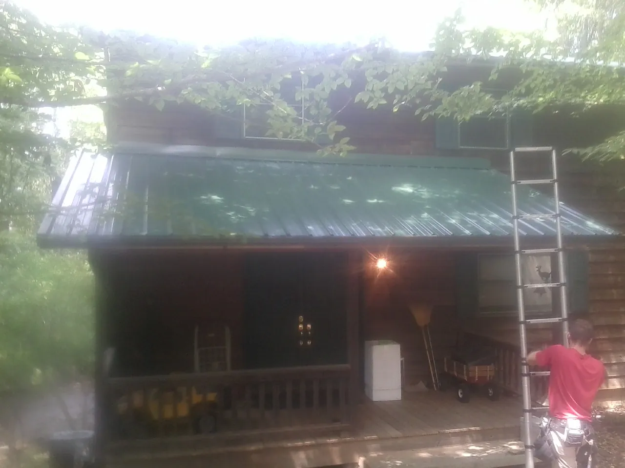 Worker on a ladder at the green porch roof of a wooded cabin in Milton